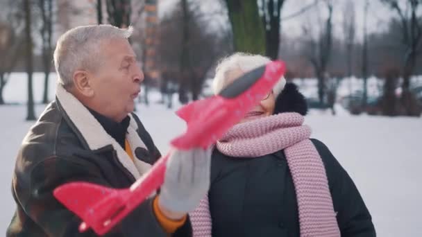 Glückliches älteres Ehepaar beim Spielen mit Flugzeugspielzeug im Park. Winterurlaubspläne — Stockvideo