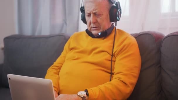 Portrét staršího muže se sluchátky hrací hry na notebooku — Stock video