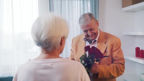 Walentynki i randki na starość. Starsza para świętuje rocznicę. Mężczyzna daje czerwone róże swojej żonie — Wideo stockowe