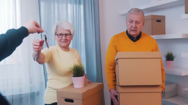 Äldre pensionerade par köper nytt hem. Kvinnan håller hus nycklar och mannen bär pappkartonger — Stockvideo