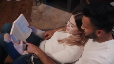 Mutlu genç, çok ırklı çift şöminenin yanında kucaklaşıp kitap okuyorlar. Kış tatili, Noel ya da sevgililer günü