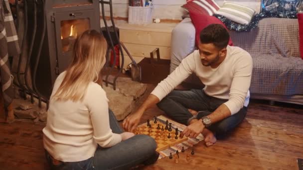 Vacances d'hiver. Heureux jeune couple multiracial jouant aux échecs dans une maison confortable près de la cheminée. Saint Valentin — Video