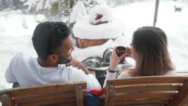 Πίσω όψη. Ευτυχισμένο νεαρό ζευγάρι πίνοντας ζεστή σοκολάτα, ενώ κάθεται στον πάγκο σε εξωτερικούς χώρους την ημέρα του Αγίου Βαλεντίνου — Αρχείο Βίντεο