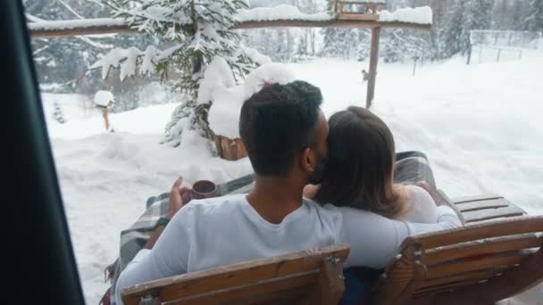 Vacances d'hiver. Jeune couple multiracial assis sur le banc et embrassant à l'extérieur. Boire une boisson chaude — Video