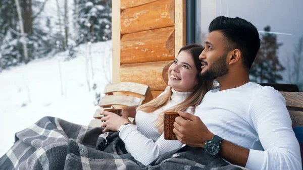 Vacaciones de invierno. Pareja joven multiracial sentada en el banco y besándose al aire libre. Beber bebidas calientes —  Fotos de Stock