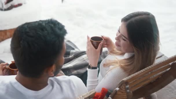 Feliz joven pareja bebiendo chocolate caliente mientras se sienta en el banco al aire libre en el día de San Valentín — Vídeos de Stock