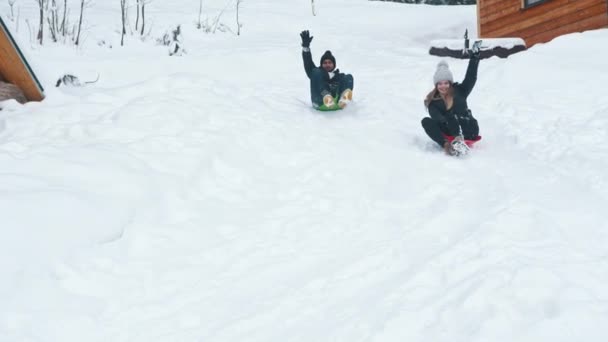 Tél a szabadban szórakozás. Fiatal férfi és nő csúszik a hóban — Stock videók