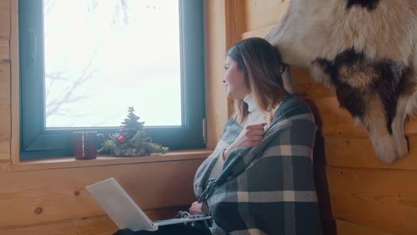 Jeune femme caucasienne assise près de la fenêtre couverte de couverture regarder à l'extérieur et à l'aide d'un ordinateur portable — Video