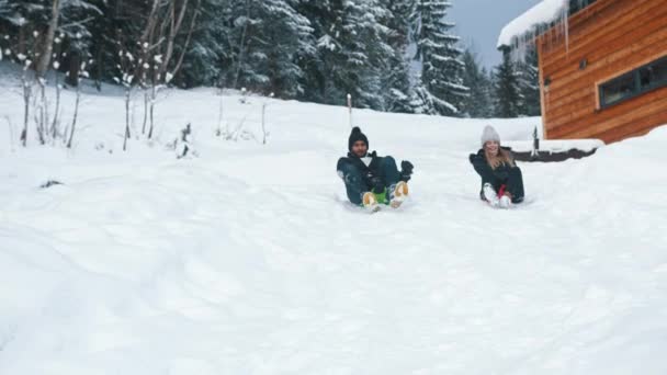 Feliz casal multirracial jovem deslizando na neve. Mulher cai — Vídeo de Stock