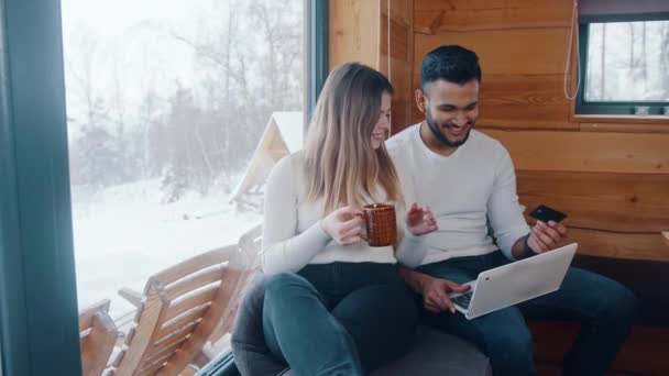 Feliz casal multirracial jovem usando cartão de crédito para fazer compras on-line. Reserva férias de inverno — Vídeo de Stock