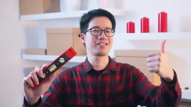 Young asian man showing thumb up and holding leveller in the other hand — Stock Video