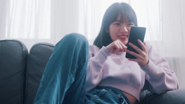 Jeune femme asiatique heureuse se détendre sur le canapé et la navigation sur les médias sociaux sur son smartphone — Video