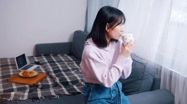 Genç yalnız Asyalı kadın sabah kahvesini içip pencereden dışarı bakıyor.