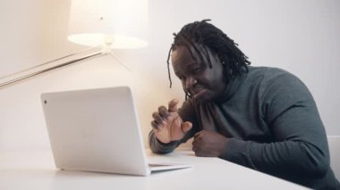 Genç Afro-Amerikan bir adam dizüstü bilgisayar kullanıyor ve videoda karısına hediyesini gösteriyor.