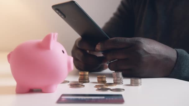 Ο άνθρωπος που χρησιμοποιεί το τηλέφωνο για να ελέγξει τον τραπεζικό του λογαριασμό. Piggy τραπεζική πιστωτική κάρτα και τα κέρματα στο τραπέζι — Αρχείο Βίντεο