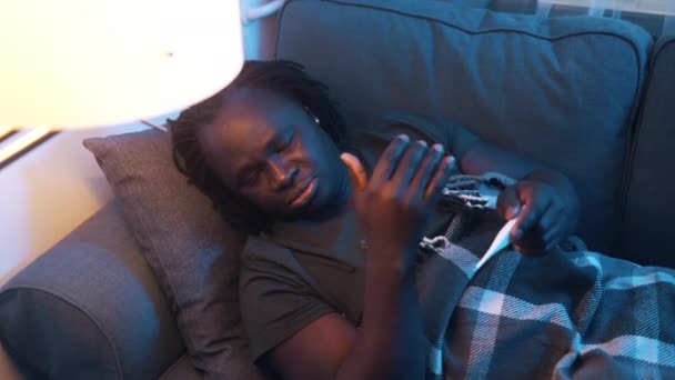 Un afroamericano enfermo girando en el sofá. Fiebre alta, enfermedad covid-19 — Vídeos de Stock