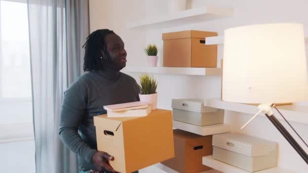 Молодой африканский американец переезжает в новую квартиру. Проведение картонных коробок и завода — стоковое видео