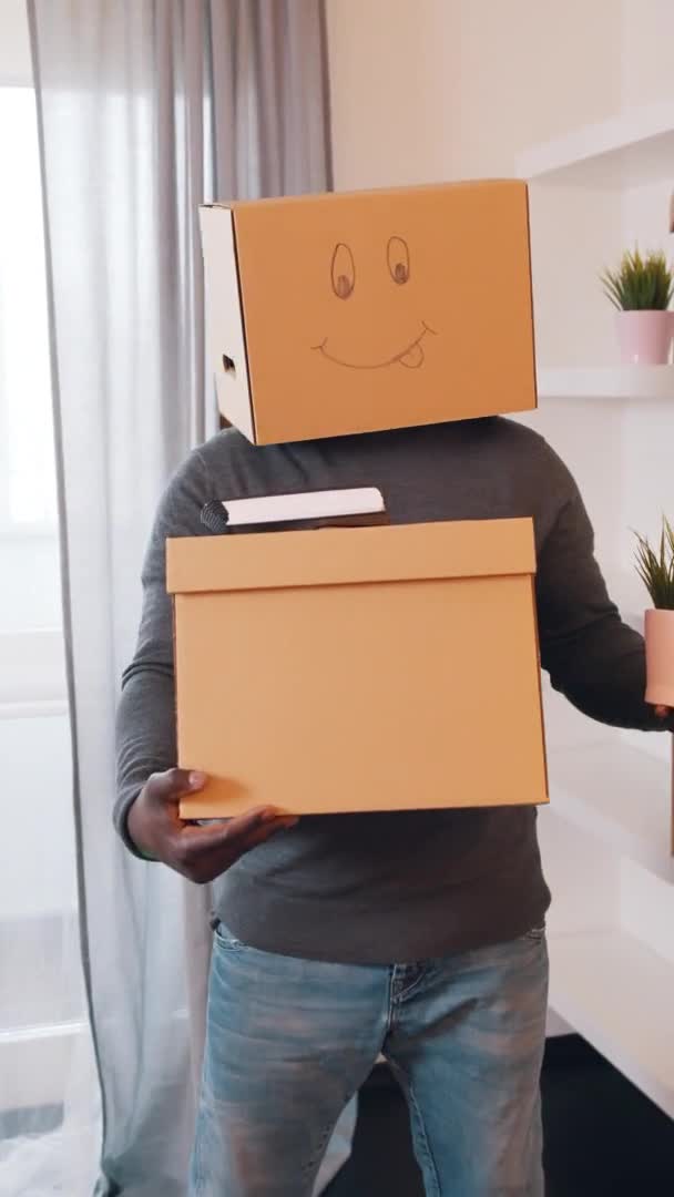Vertikal, oigenkännlig svart man med pappkartong på huvudet flyttar i ny lägenhet — Stockvideo