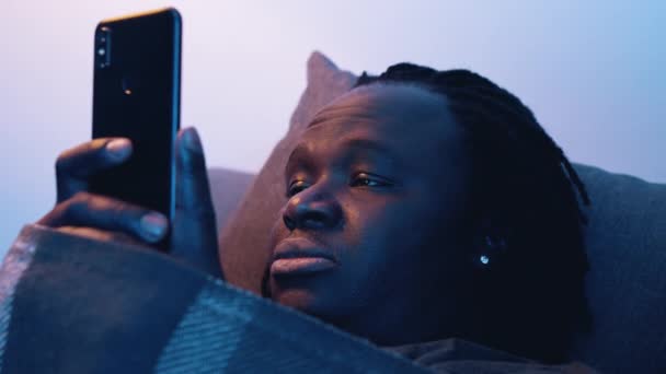 Africain américain fatigué homme noir tenant smartphone tout en étant couché sur le canapé — Video