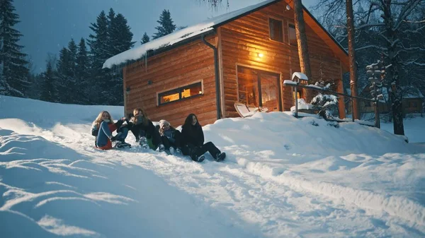 Best friends sliding on the sleds downhill in front of the wooden house. Winter season, Christmas holidays
