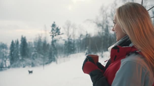 Młoda blondynka pijąca gorący napój i ciesząca się opadami śniegu na górze — Wideo stockowe