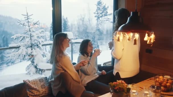 Glückliche junge Frauen feiern das neue Jahr in einer Berghütte aus Holz. Entspannen am Fenster mit Heißgetränk — Stockvideo