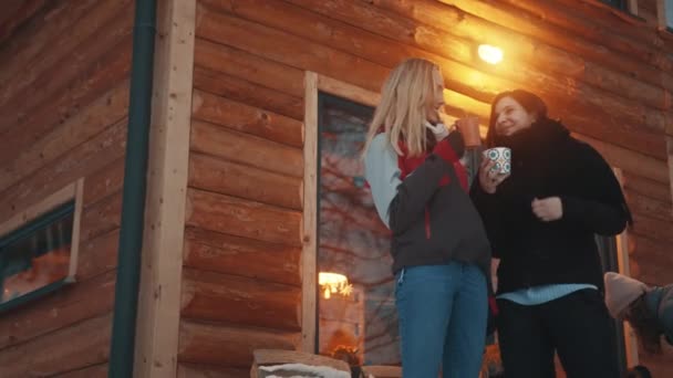 Beste Freunde, die Spaß am Berg haben und Winterurlaub feiern. Heißer Tee vor dem Holzhaus trinken — Stockvideo