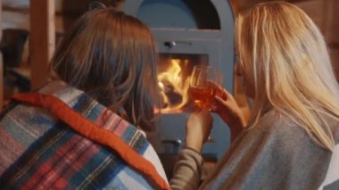 İki genç kadın, lezbiyen çift şöminenin yanında dinleniyor ve rahat bir evde şarap içiyorlar.