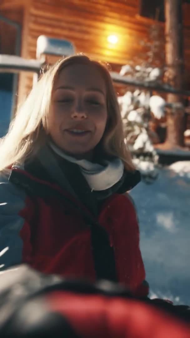 Pionowe. Podekscytowana młoda kobieta influencer nagrywania wideo przed górskim drewnianym domu na śniegu evenng — Wideo stockowe