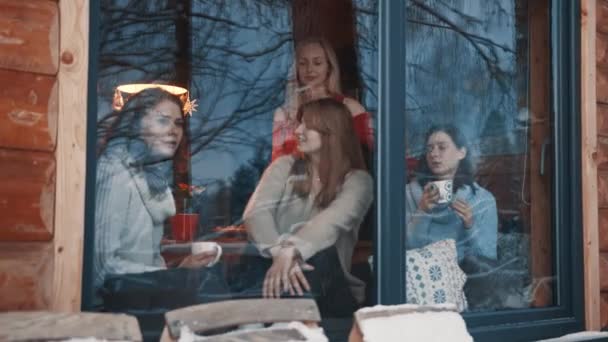 Frauen, beste Freundinnen, die Winterurlaub im Berghaus aus Holz verbringen. Heißgetränke trinken und am großen Fenster plaudern — Stockvideo