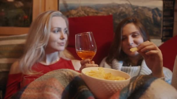 Giovani donne che si rilassano sul divano coperto di coperta bevendo vin brulè e facendo uno spuntino — Video Stock