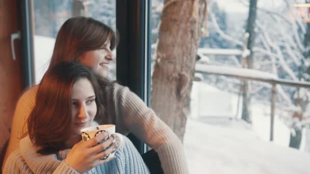 Dvě módní krásné lesbičky dívky sedí u okna a popíjejí kávu. — Stock video