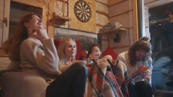 Las mejores amigas pasan las vacaciones de invierno en la acogedora casa bebiendo vino caliente con especias y comiendo bocadillos. — Vídeos de Stock