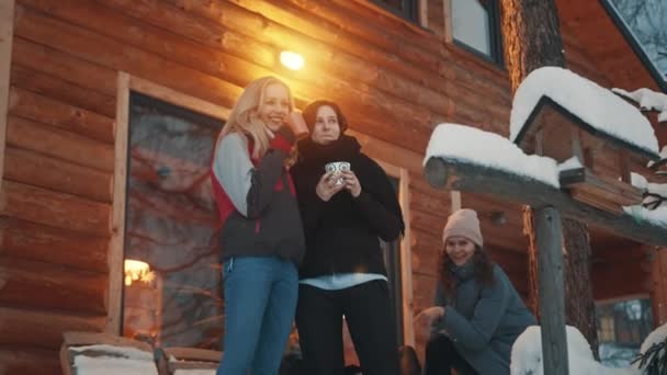 Kobiety spędzają zimowe wakacje w górach. Picie gorącego napoju przed drewnianym domem i korzystających z opadów śniegu — Wideo stockowe