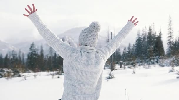 Jovem mulher acariciando a queda de neve e levantando as mãos na montanha — Vídeo de Stock