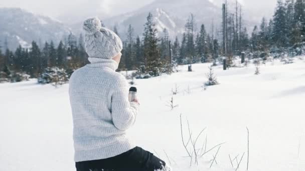 Jovem em férias de inverno na montanha. Beber bebida quente da garrafa térmica e desfrutar de neve — Vídeo de Stock