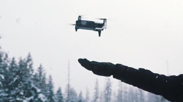 Drone pousando na mão do proprietário no dia de inverno nevado. Montanha floresta de pinheiros no fundo — Vídeo de Stock