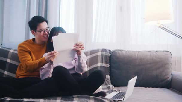 Feliz jovem casal relaxante no sofá e olhando para papéis — Vídeo de Stock