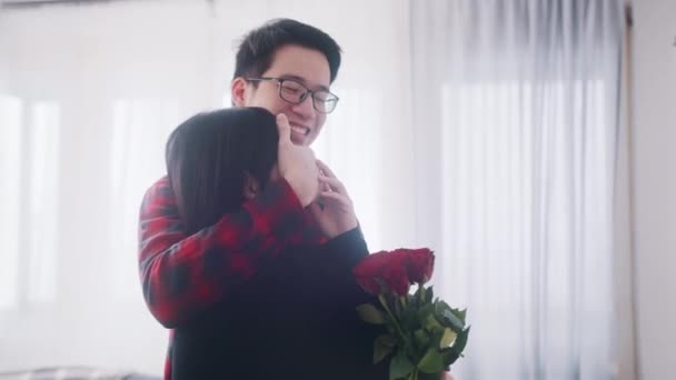 Молодий азіатський чоловік закриває очі своєї дівчини і дивує її червоними трояндами на ювілей — стокове відео