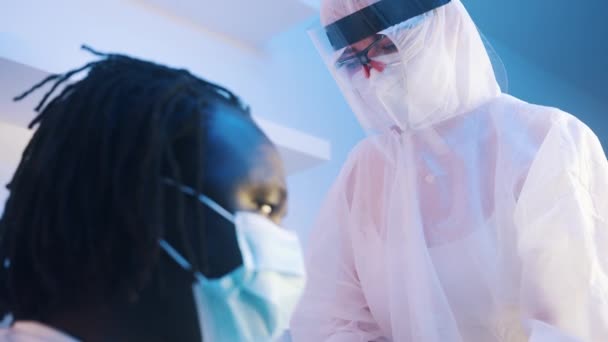 Медсестра в защитном костюме дает вакцину против коронавируса африканскому чернокожему мужчине — стоковое видео