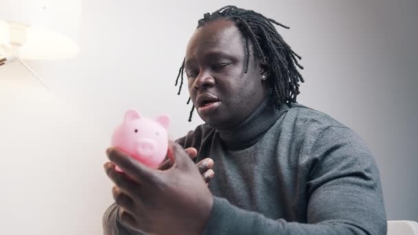 Konkurskonzept. Trauriger afrikanisch-amerikanischer Schwarzer blickt auf leeres Sparschwein und schüttelt den Kopf — Stockvideo