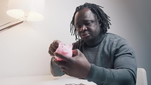 Investitionen und Wohlstandswachstum. Afrikanischer Schwarzer legt Münzen ins Sparschwein — Stockvideo