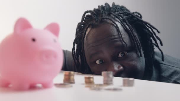 Decisión financiera, inversiones y ahorros. Un hombre gracioso mirando las monedas frente a la alcancía. Concentración de estanterías — Vídeos de Stock