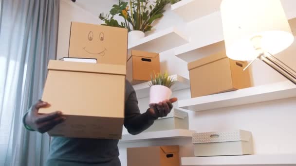 Emocionado hombre negro con caja de cartón sobre su cabeza reubicándose en un nuevo hogar — Vídeo de stock