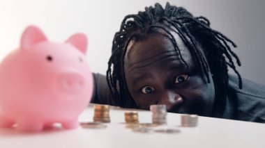 Adam birikimlerini sayıyor. Etrafı bozuk paralarla çevrili bir kumbara. Yatırım kararı