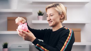 Domuz kumbarasına bozuk para koyan mutlu beyaz kadının portresi.