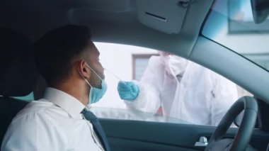 PPE 'de çalışan bir tıp çalışanı arabadaki kişiye burun ve boğaz temizliği yapıyor.