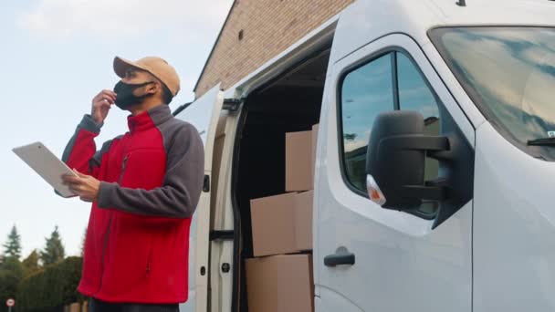 Junger Mann vor Lieferwagen bei der Überprüfung des Pakets mit digitalem Tablet und Gesichtsmaske — Stockvideo