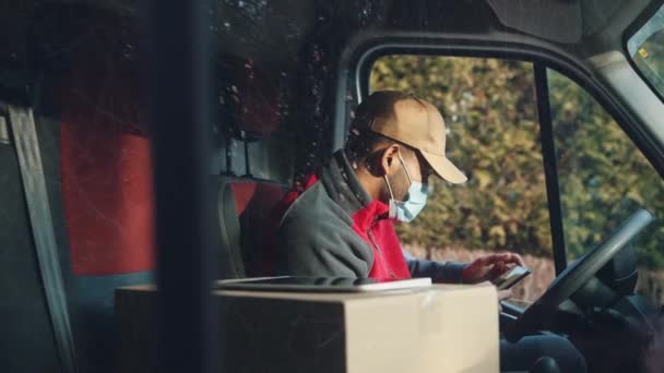 Kurier prüft Karte auf dem Smartphone auf dem Fahrersitz. Mann mit Gesichtsmaske liefert Paket ab — Stockvideo