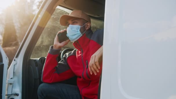 Man met medisch masker zittend op de bestuurdersstoel van het busje en een telefoontje — Stockvideo